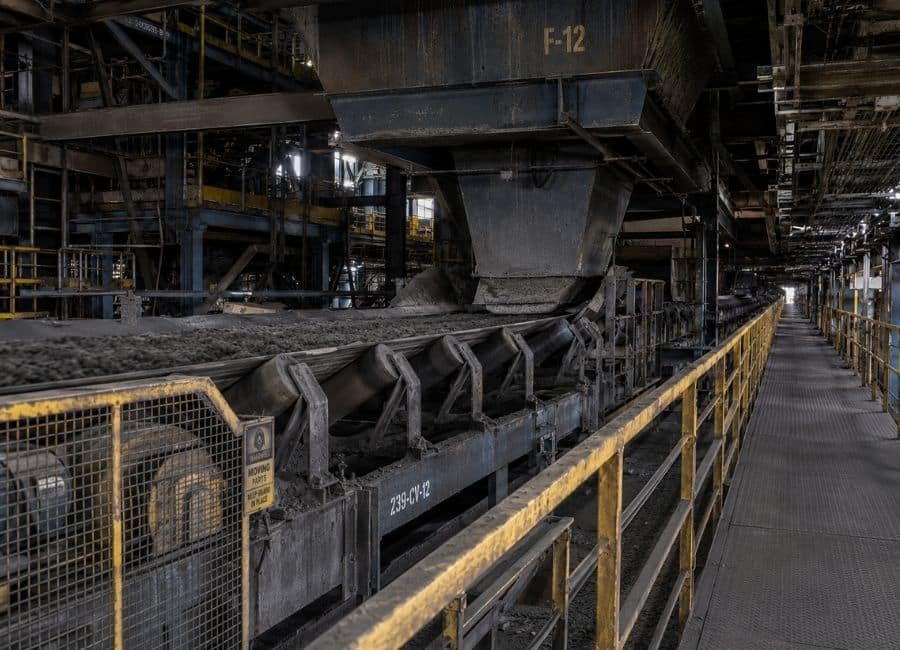 Dark industrial conveyor system carrying material through a processing facility, with text reading Where Performance Leaks Away, representing hidden output loss, throughput pressure and performance drift in industrial operations.